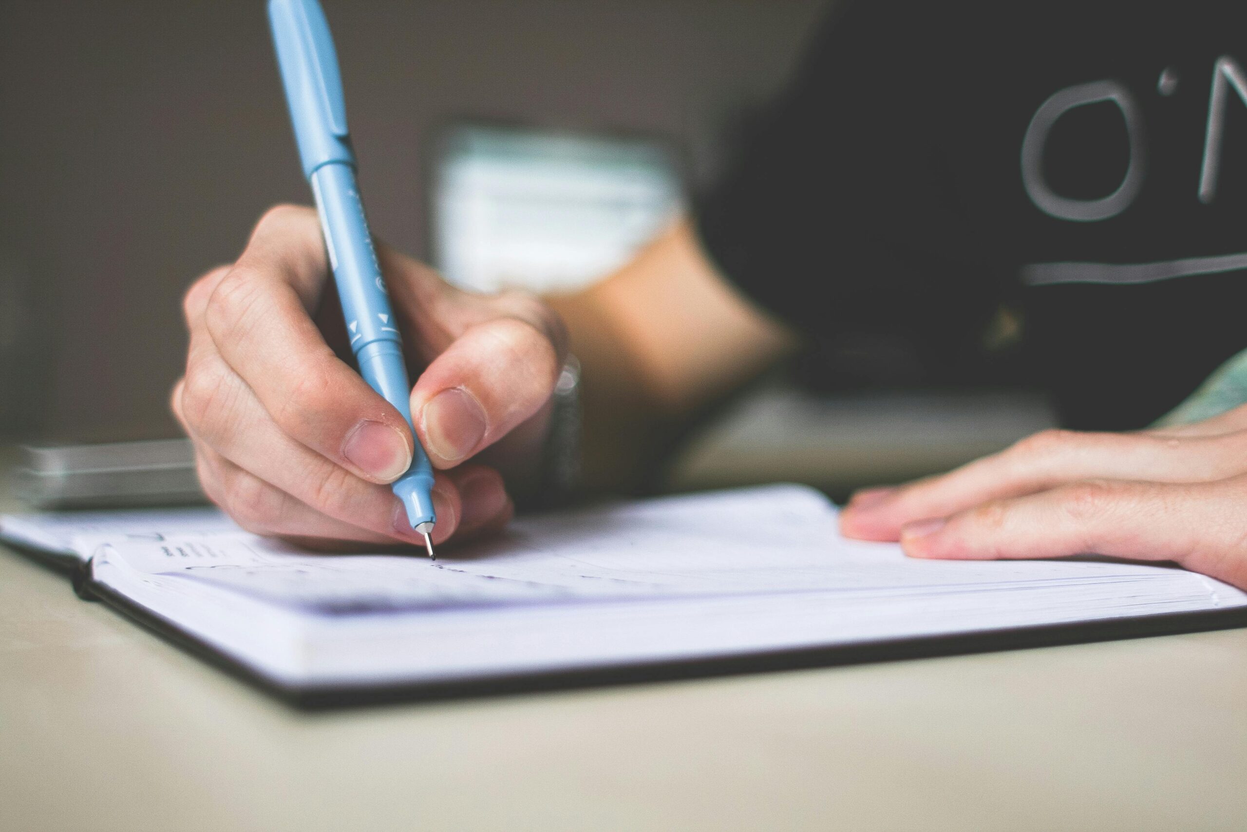 UNA MANO CON UNA PLUMA ESCRIBIENDO EN UNA LIBRETA